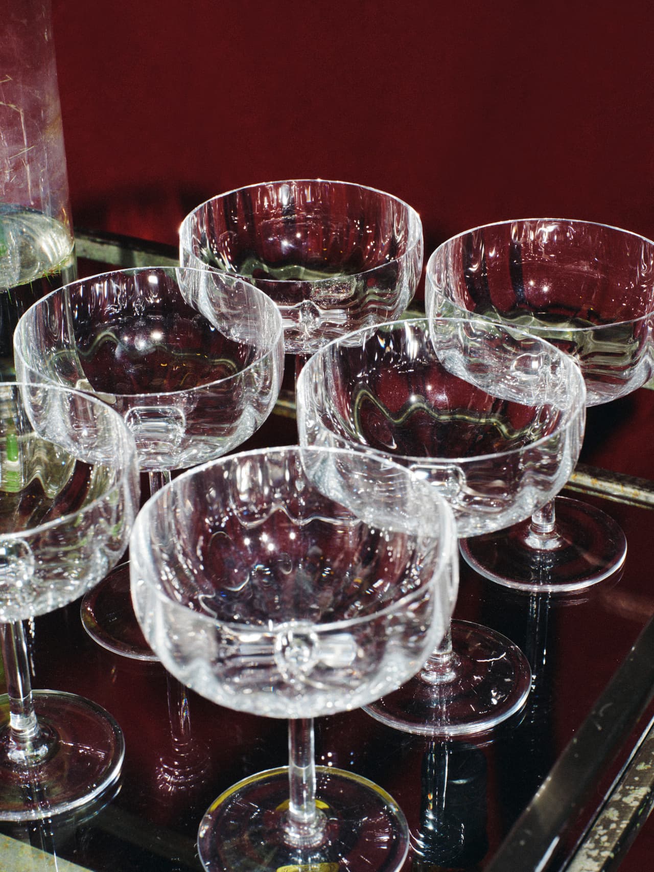 six empty coupe glasses on a glass tray against a red velvet wall, flash