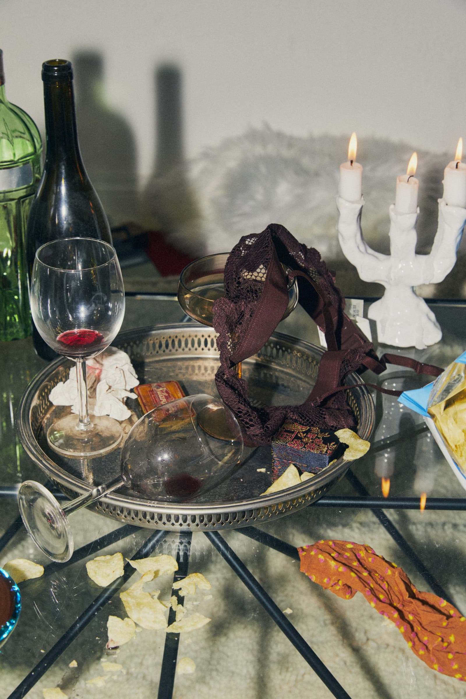 fallen wine glass, lace bra and crisps on a silver tray, candles lit, flash